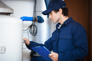 An HVAC technician in a blue uniform is inspecting a water heater