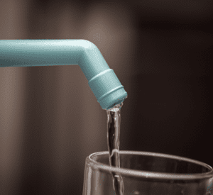 Close-up of water pouring from a blue water filter pipe into a glass