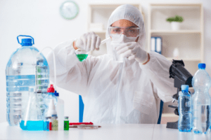 A scientist in protective gear conducts a water quality test, pouring liquid from one container to another