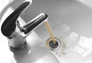 A faucet flows brown, contaminated water into a sink basin.